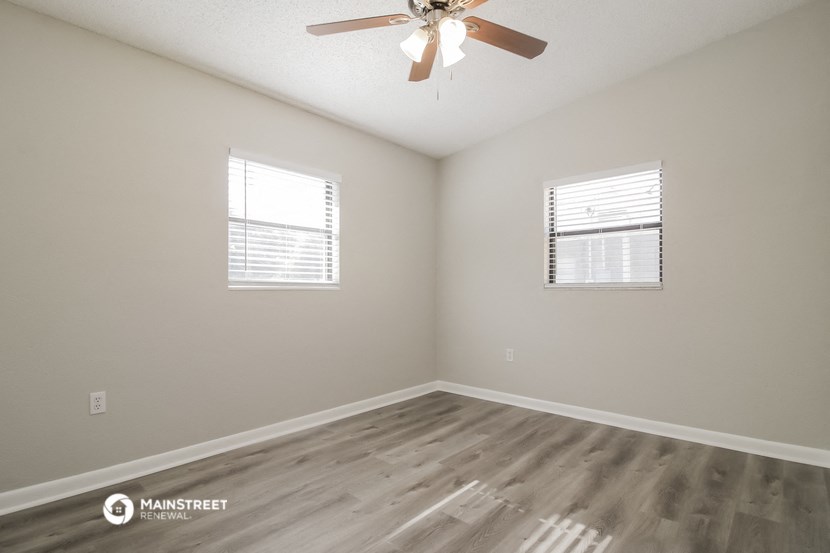 an empty bedroom with a ceiling fan and two windows