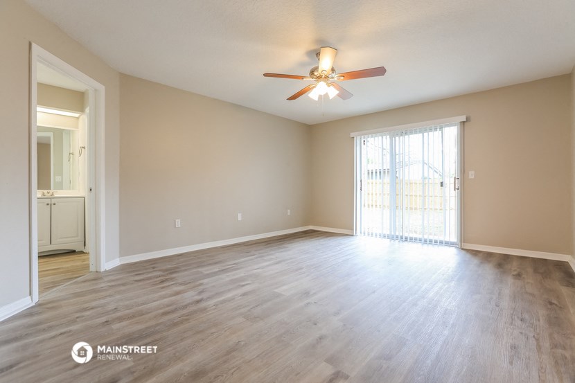 the spacious living room with wood flooring and a ceiling fan