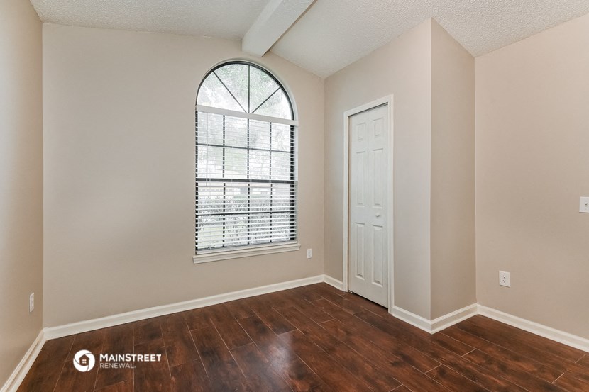 the spacious living room with a large arched window and wood flooring