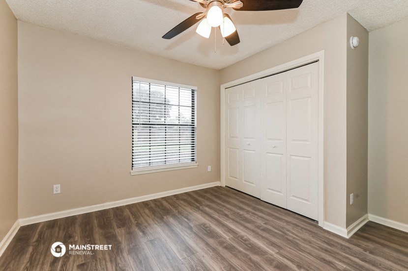 the spacious living room of an empty home with a ceiling fan and a closet