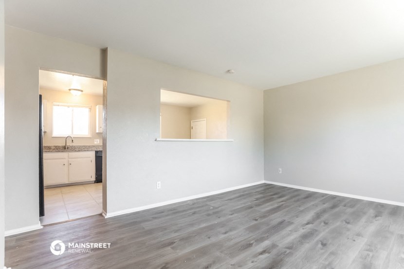 an empty living room with wood flooring and a kitchen