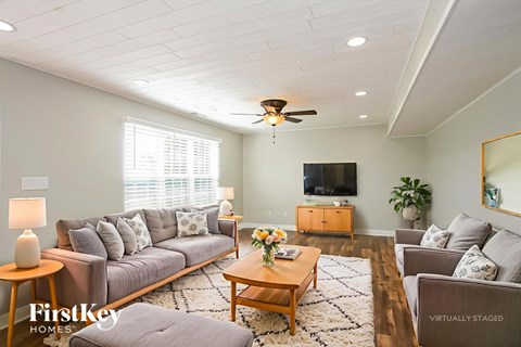 A living room with a grey couch, a wooden coffee table, a flat screen TV, and a ceiling fan.