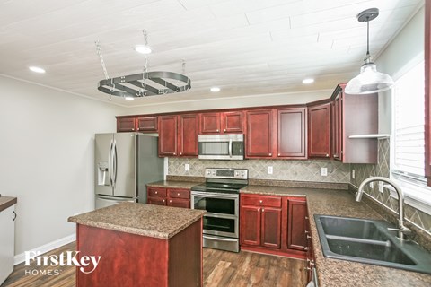 A kitchen with red cabinets and a granite island.