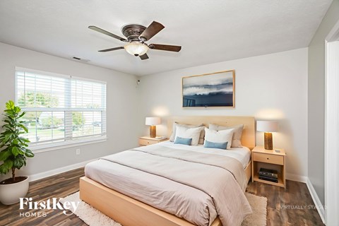 A bedroom with a bed, a ceiling fan, and a painting on the wall.