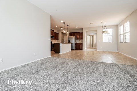 A spacious living room with a grey carpet and a kitchen in the background.