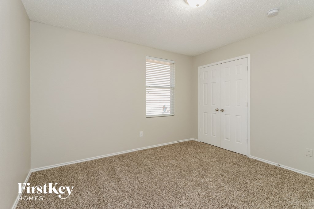 A carpeted room with a door and a window with blinds.