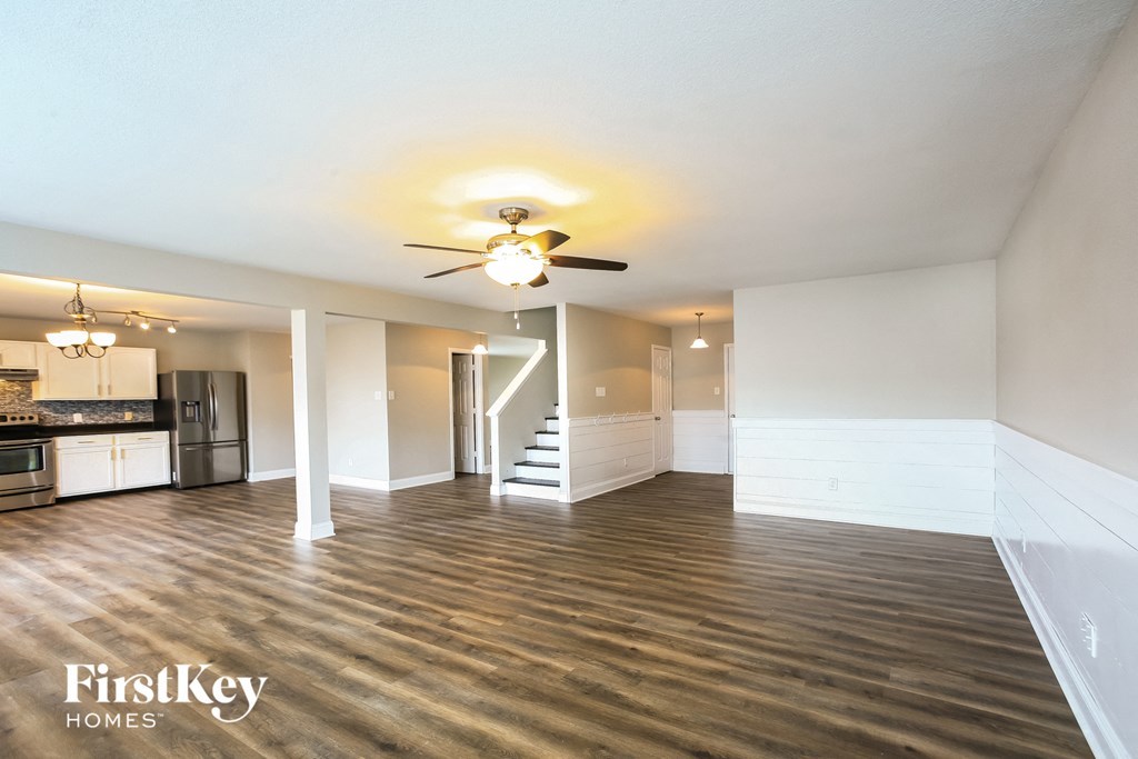 an empty living room with a ceiling fan and a kitchen