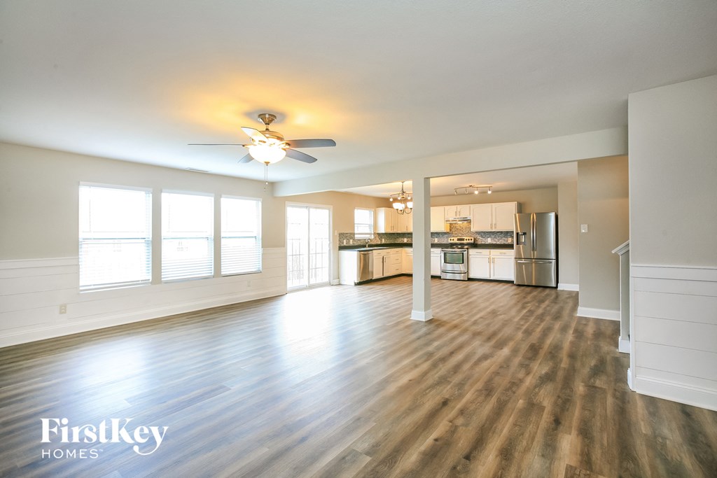 an empty living room with a ceiling fan and a kitchen