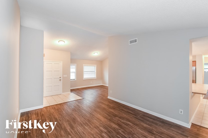 A spacious room with wooden floors and white walls, with a door on the left and a window on the right.