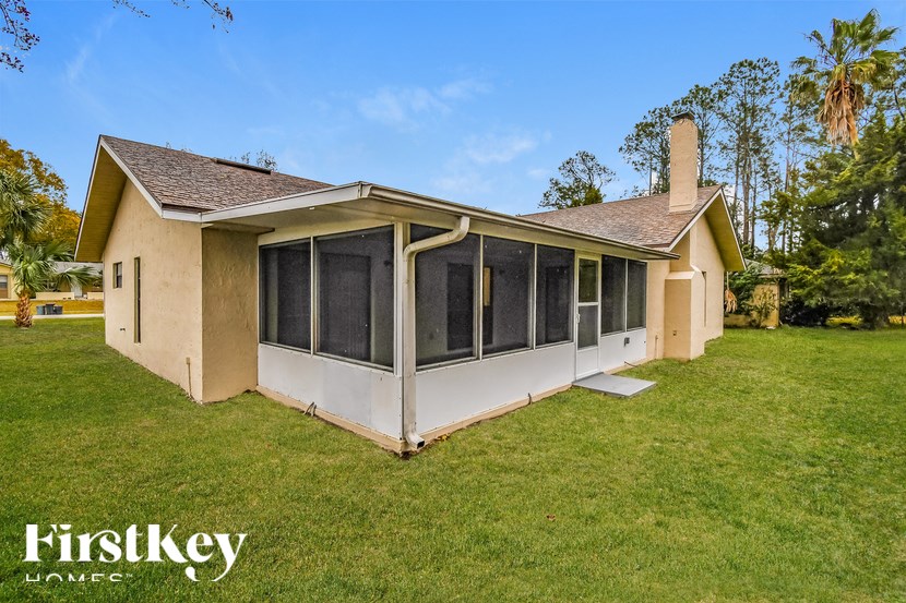 A house with a brown roof and a white exterior is surrounded by a grassy lawn.