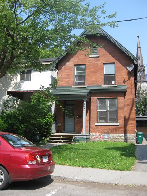 A red car is parked in front of a brick house.