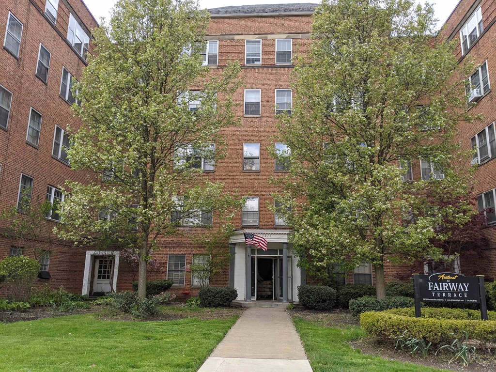 an apartment building with a sidewalk and trees in front of it