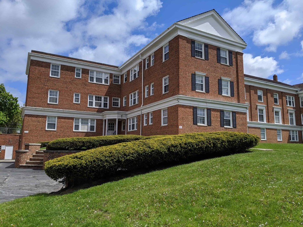 the front of a brick building with a lawn and bushes