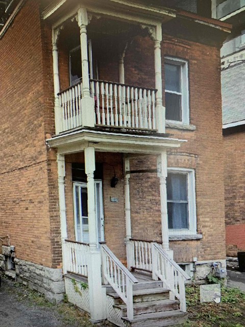 A two-story brick house with a balcony and stairs leading to the front door.