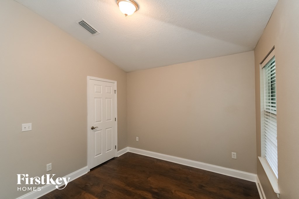 a bedroom with a white door and wood flooring and a window