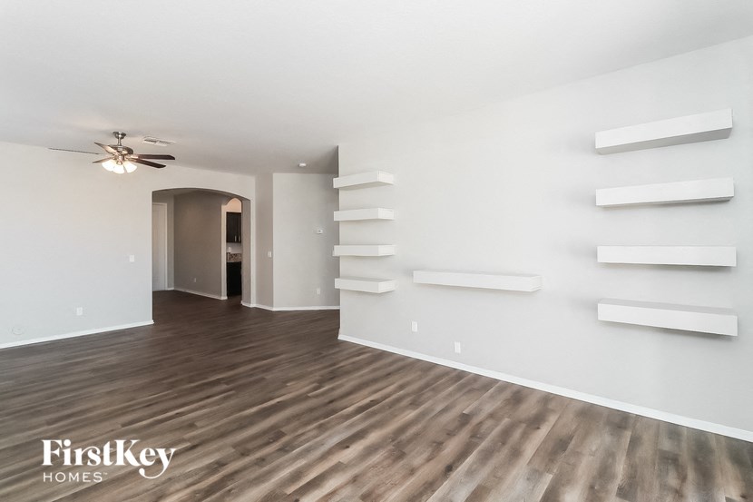 A spacious room with wooden flooring and white walls, featuring a ceiling fan and built-in shelves.