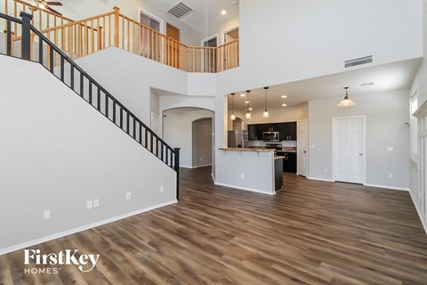 A spacious living room with a kitchen in the background and a staircase with a railing on the left side.
