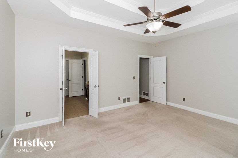 a empty living room with a ceiling fan and a door to a hallway