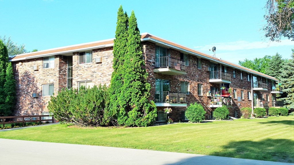 a large brick apartment building with a green lawn and trees