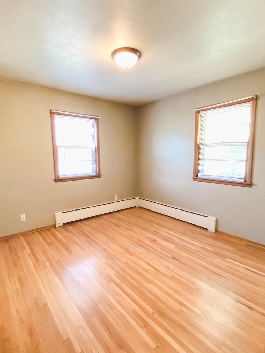 an empty living room with wood floors and two windows