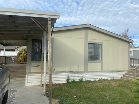 A mobile home with a covered porch and a car parked in front.