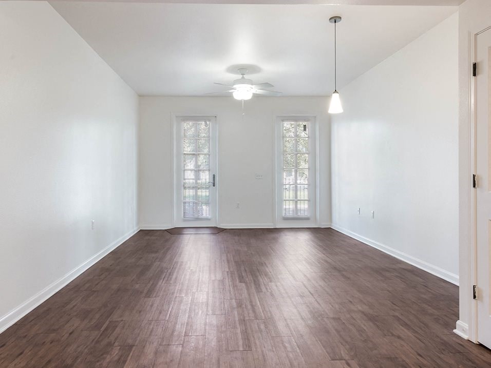 an empty living room with wood floors and a ceiling fan