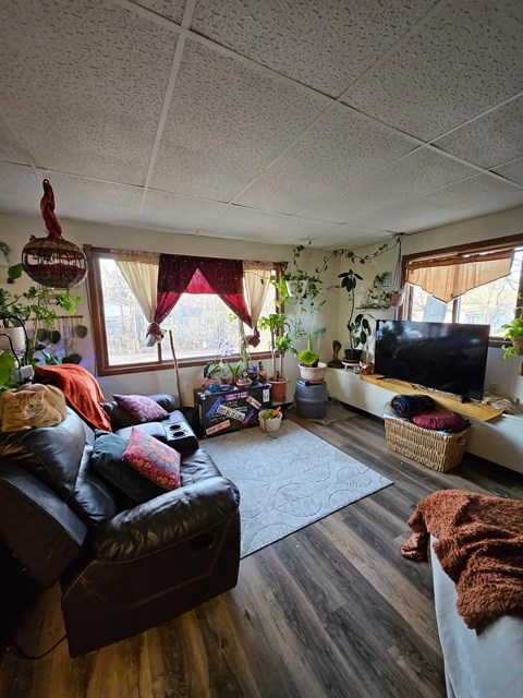 A living room with a black leather couch and a wooden floor.