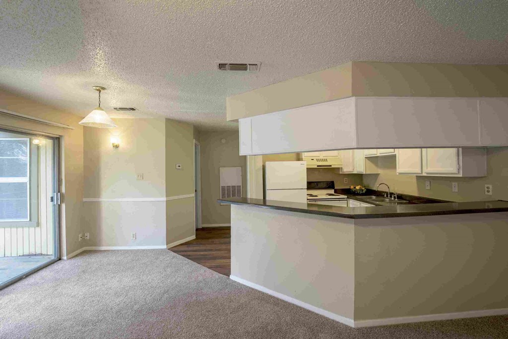 an empty living room with a kitchen with a counter top