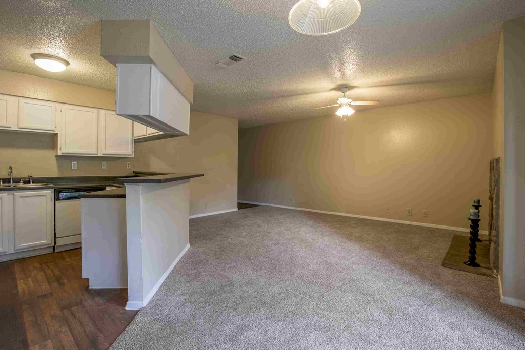 an empty living room with a kitchen with a counter top and