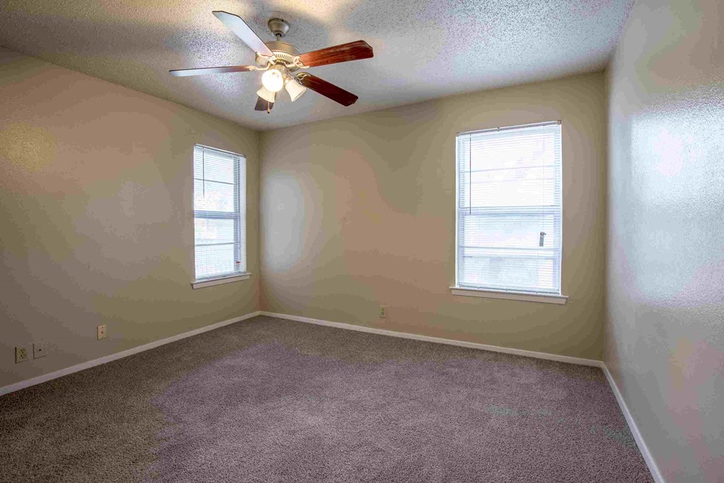 an empty room with a ceiling fan and two windows