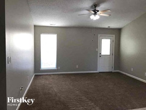 A room with a carpeted floor, a ceiling fan, and a door.