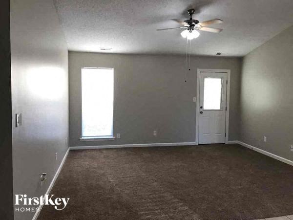 A room with a carpeted floor, a ceiling fan, and a door.