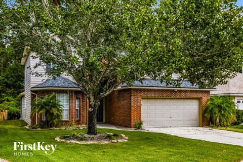 a white garage door in front of a brick house with a tree