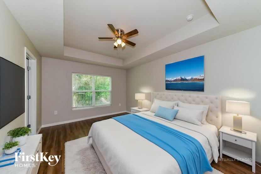 A bedroom with a bed, a ceiling fan, and a painting of a mountain landscape on the wall.