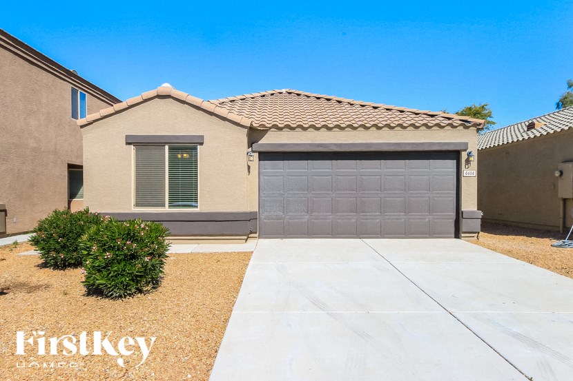A house with a garage door and a small bush in front of it.