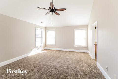 a carpeted living room with a ceiling fan and two windows
