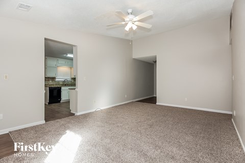 a spacious living room with carpet and a ceiling fan