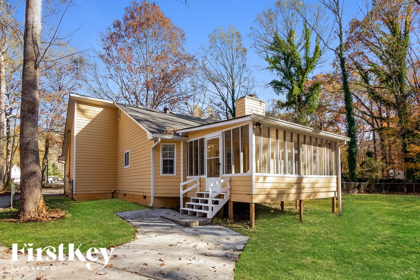 A house with a beige exterior and a white porch is surrounded by trees.