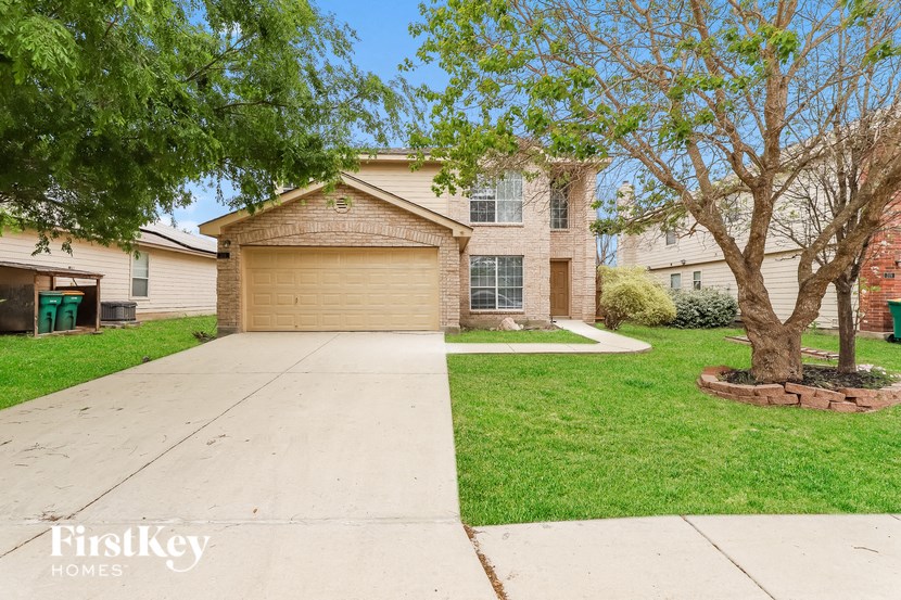 a beige brick house with a driveway and trees