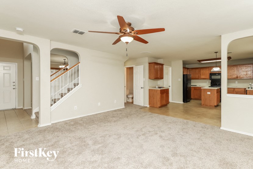 an empty living room with a ceiling fan and a kitchen