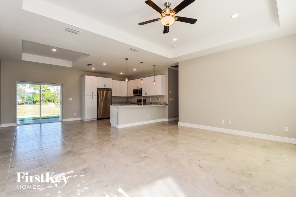 A spacious kitchen and living room with a ceiling fan and marble flooring.