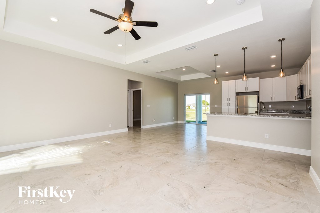 A spacious, empty room with a ceiling fan and pendant lights.