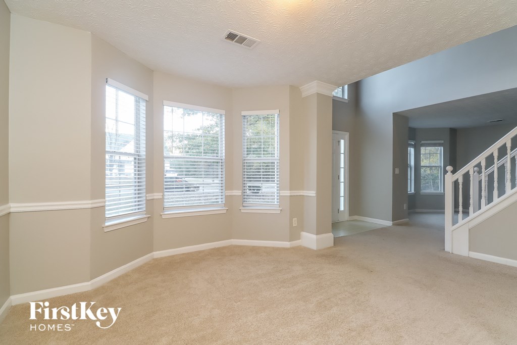 an empty living room with three windows and a staircase