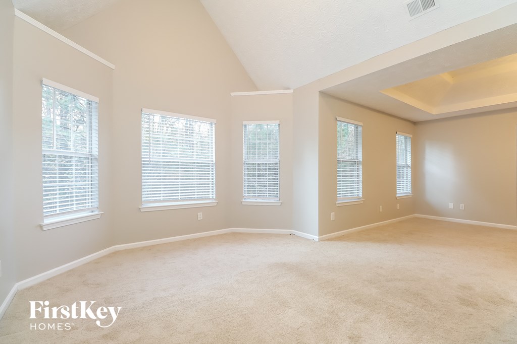 a spacious living room with three windows and a carpeted floor