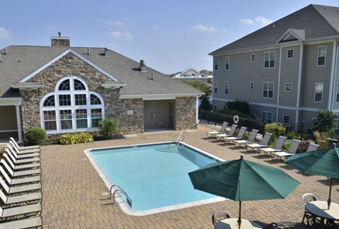 a swimming pool with chairs and umbrellas in front of a house