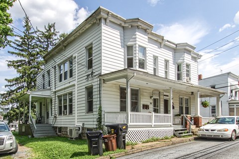 A white two-story house with a porch and a car parked in front.