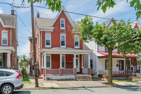 a red brick house with a white porch and a car parked in front