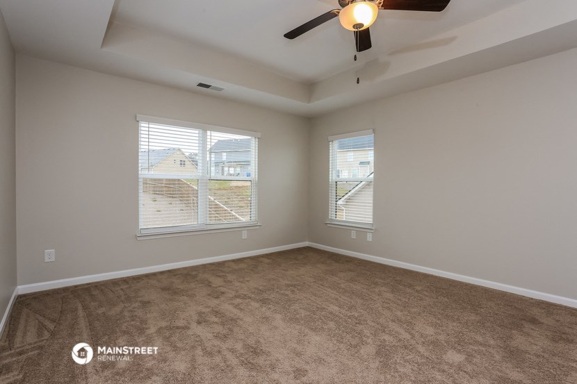 an empty living room with two windows and a ceiling fan