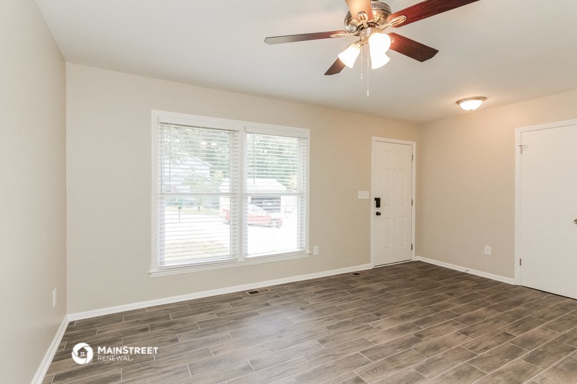 the spacious living room with wood flooring and a ceiling fan