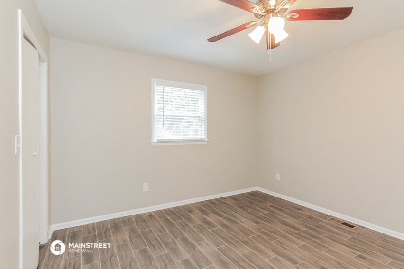 the spacious living room with wood flooring and a ceiling fan
